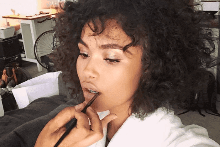 Woman applying nude lipstick with finger to create wine-stained lip effect