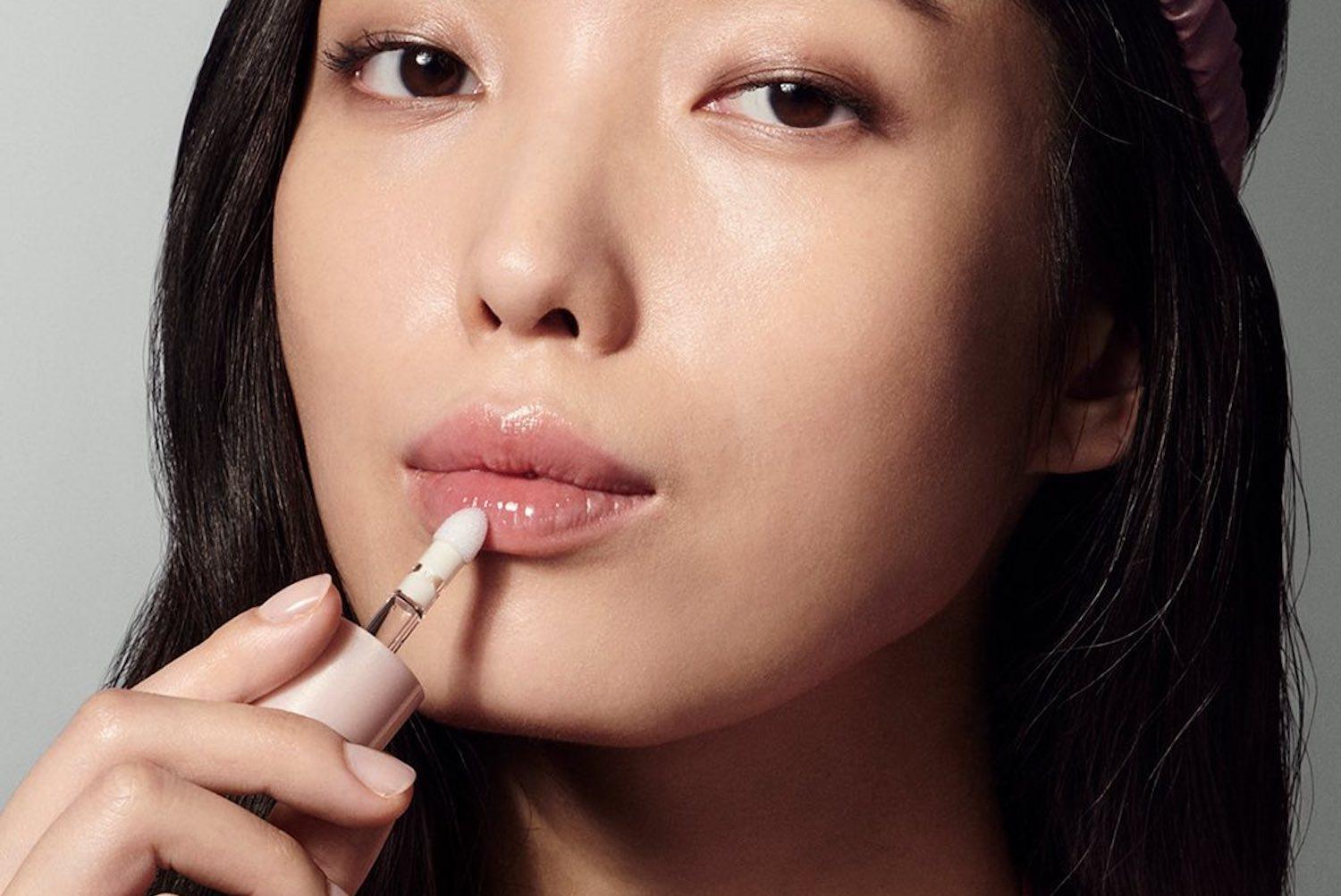 Luxury lip treatment products including oils, butters and serums in various applicator styles arranged on a neutral surface