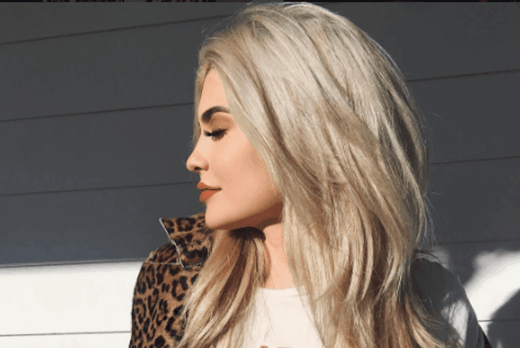 Woman with platinum blonde hair looking uncertain, touching her locks with regretful expression