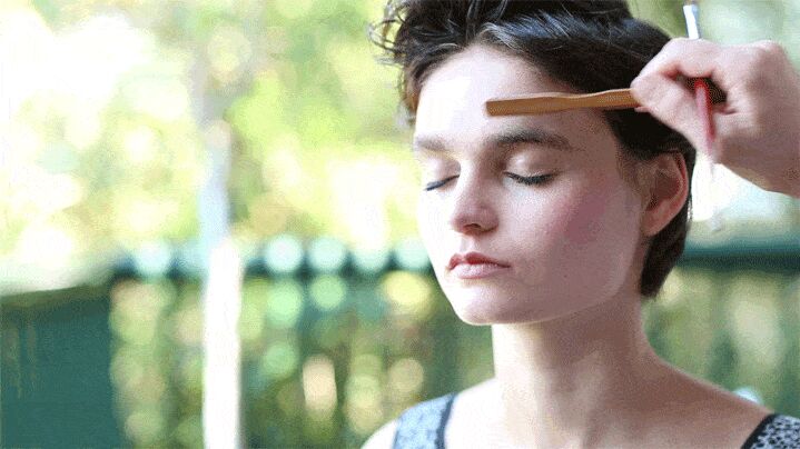 Makeup artist applying eyebrow powder to model's brow using angled brush technique