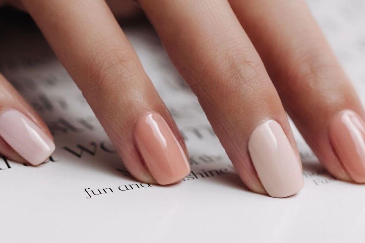 Woman applying gel nail polish with UV lamp and professional manicure tools on marble surface