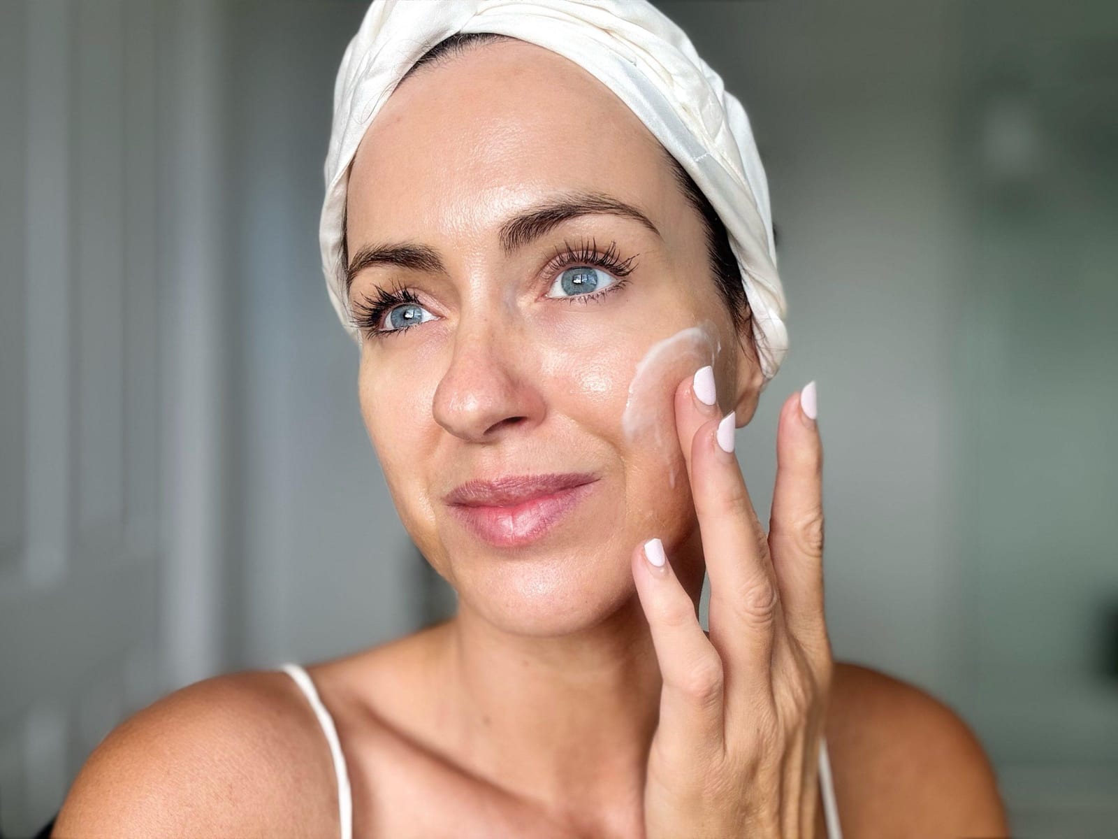 Woman applying water-cream mask by the pool in natural garden setting, wearing spa skincare