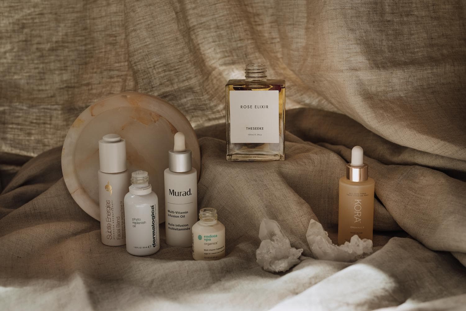 Luxury facial oils in glass bottles arranged on marble surface with winter botanicals and rose buds