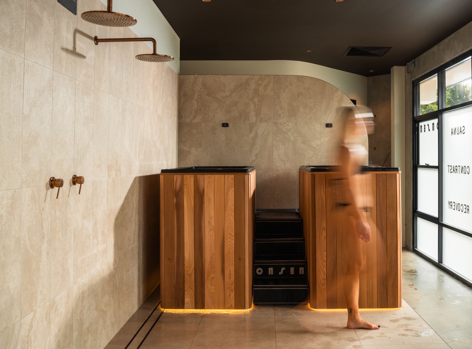 Timber compression therapy pods beside a travertine shower wall at Onsen, Torrensville