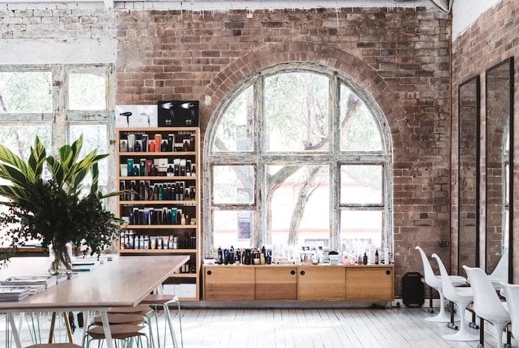 Bright, minimalist hair salon interior with vaulted ceilings, white flooring, natural light and communal wooden table