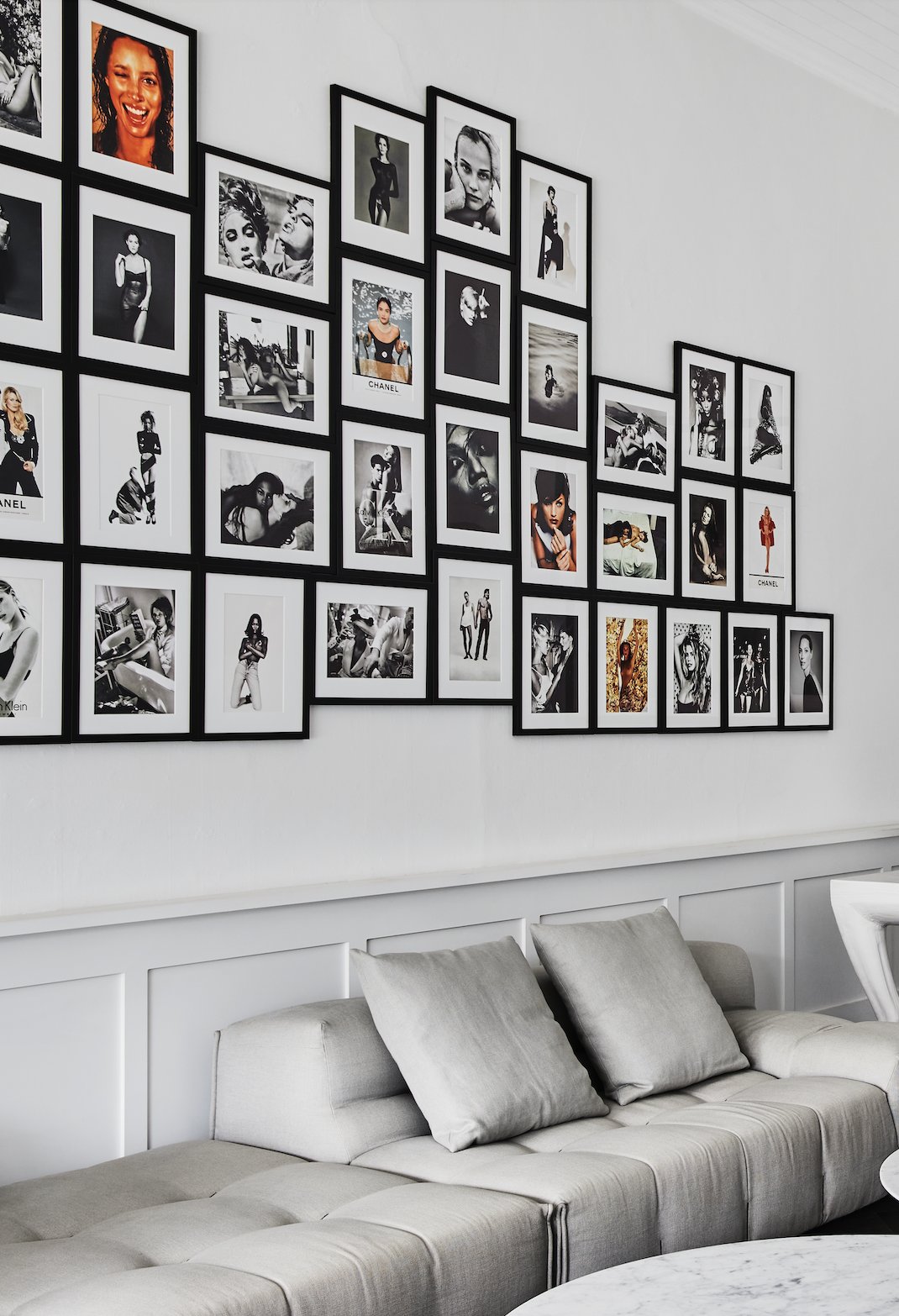 Gallery wall of framed black-and-white fashion photographs above a grey sofa at Melanie Grant Skin Health, Double Bay