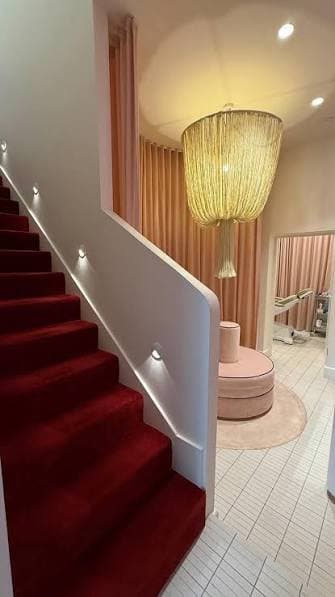 Red-carpeted staircase beside a fringe chandelier and pink curtains at Rêve Skin + Beauty, Annandale
