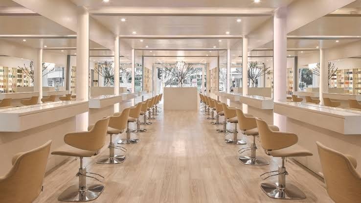 Long salon floor with white styling stations, beige chairs and potted trees at Paloma, Paddington