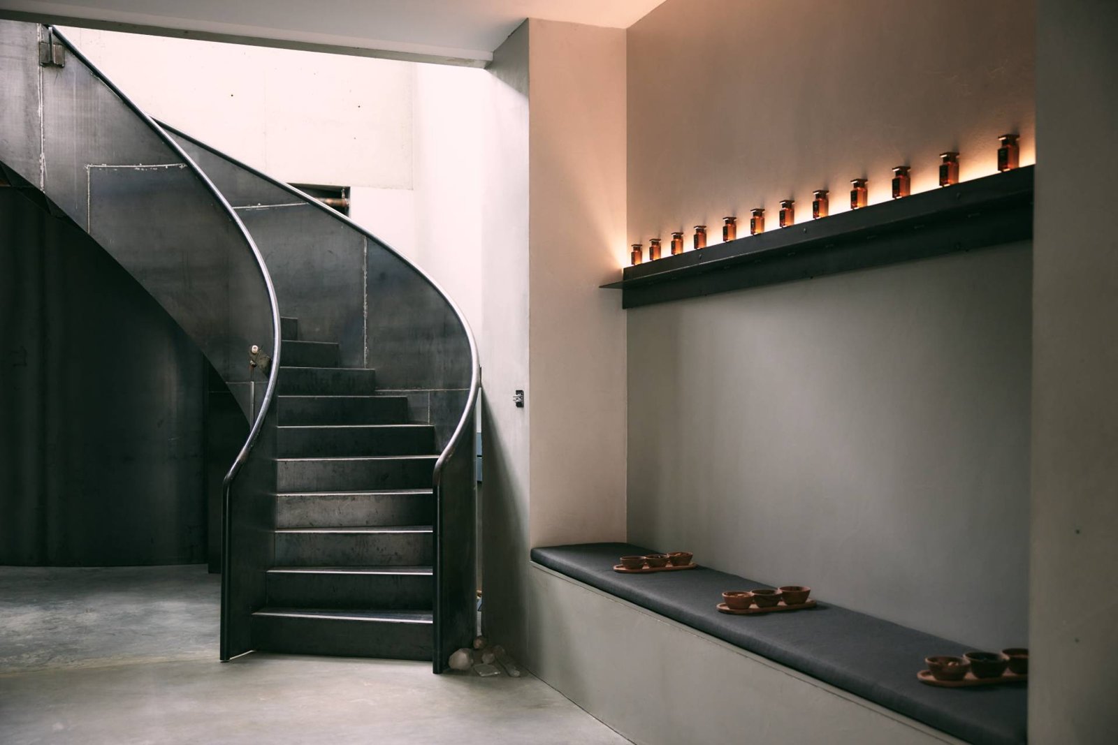 Steel spiral staircase and a bench beneath a shelf of amber glass jars at Venustus, Paddington