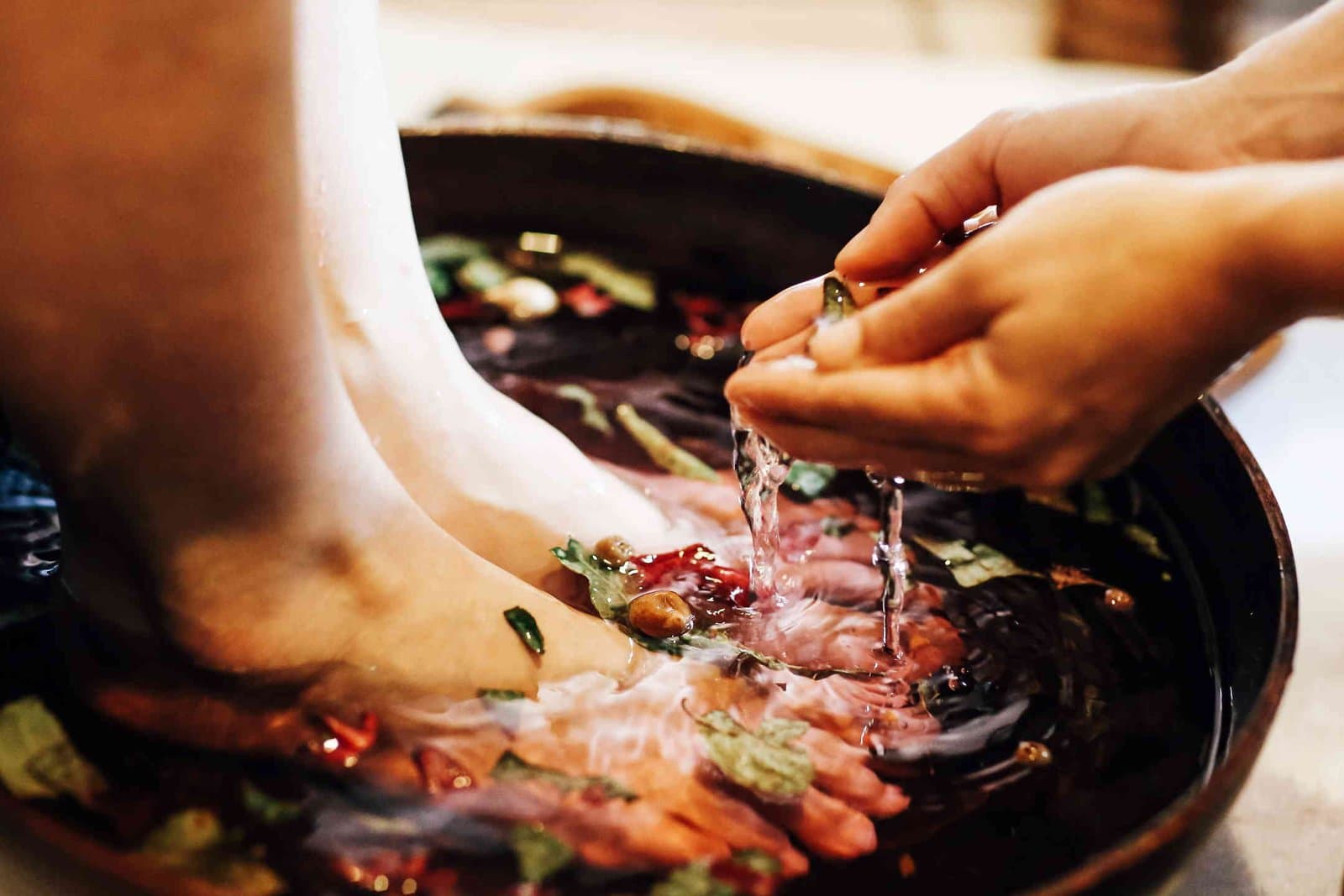 A therapist washes a guest's feet in a stone bowl scattered with petals during a spa ritual at Daintree EcoLodge