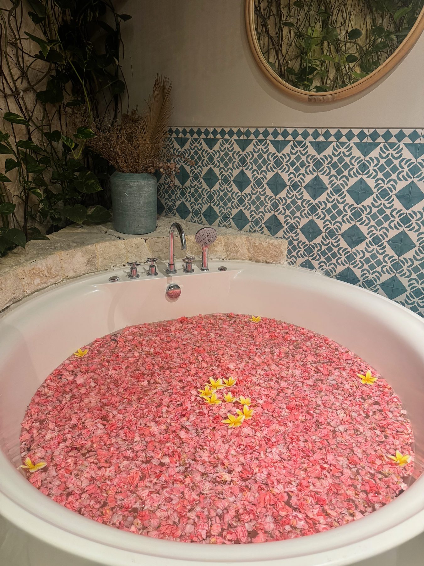 The flower bath at Escape Haven women's retreat in Canggu, Bali, a round tub filled with pink petals and frangipani against blue Moroccan tiles