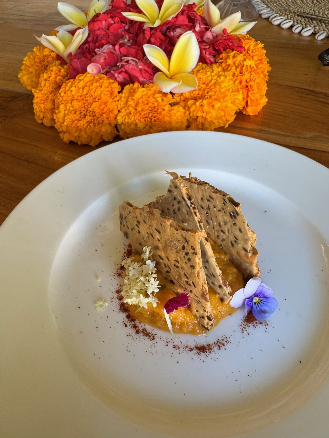 An Ayurvedic dish plated with seeded crisps and edible flowers at Escape Haven, a marigold offering behind it