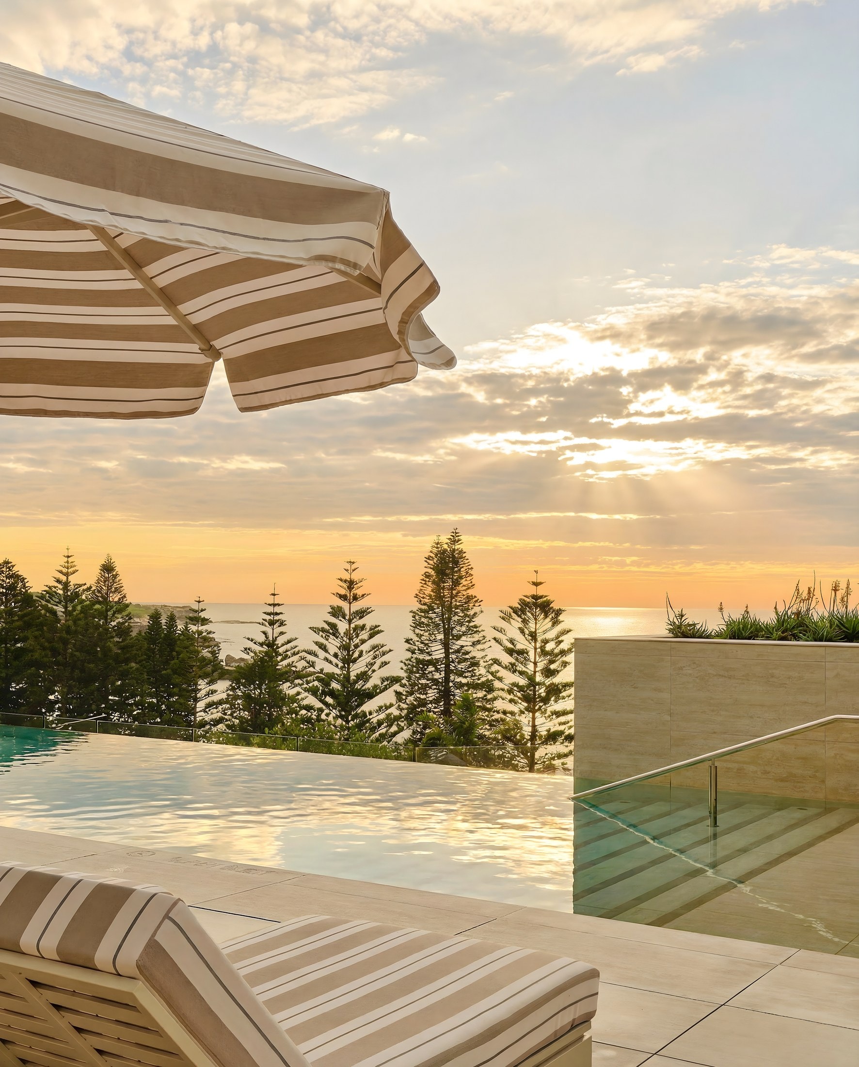 Striped umbrella and daybed beside the oceanfront infinity pool at sunrise, InterContinental Sydney Coogee Beach