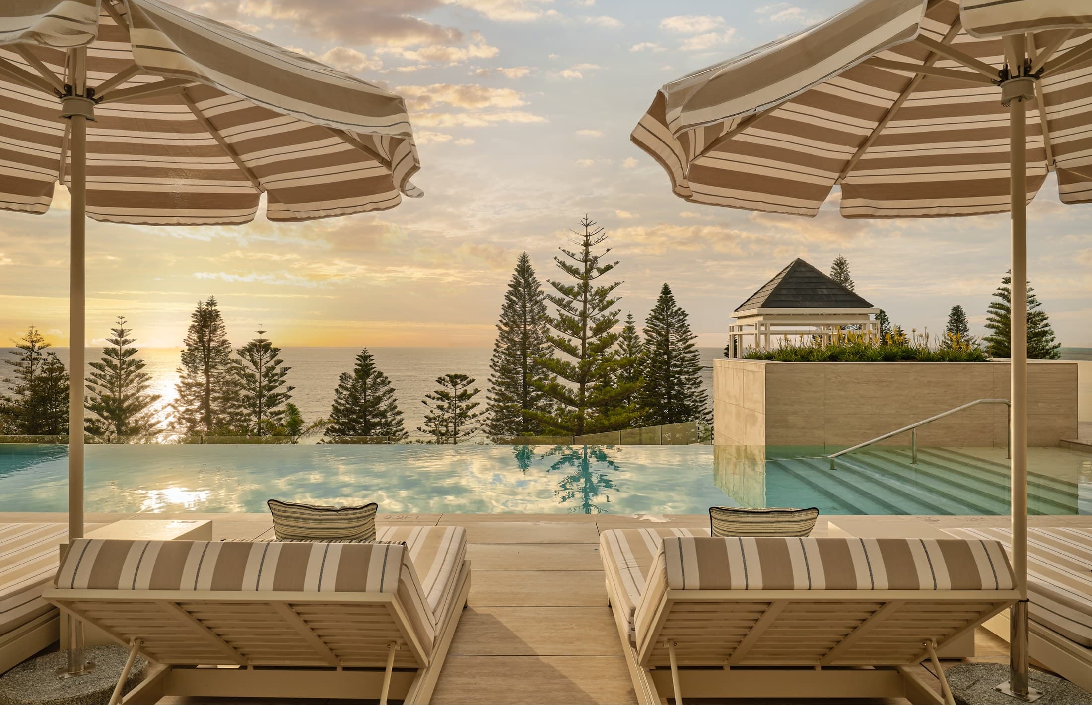 Striped umbrella and daybed beside the oceanfront infinity pool at sunrise, InterContinental Sydney Coogee Beach