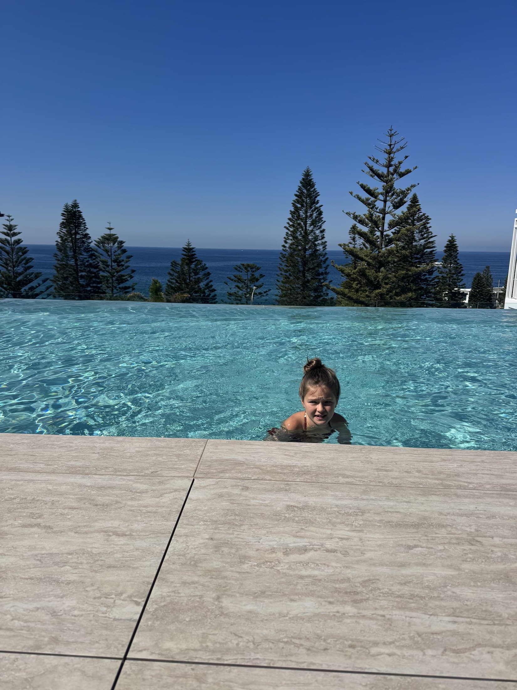 Lulu swimming in the heated infinity pool at InterContinental Sydney Coogee Beach, Norfolk pines and the ocean behind