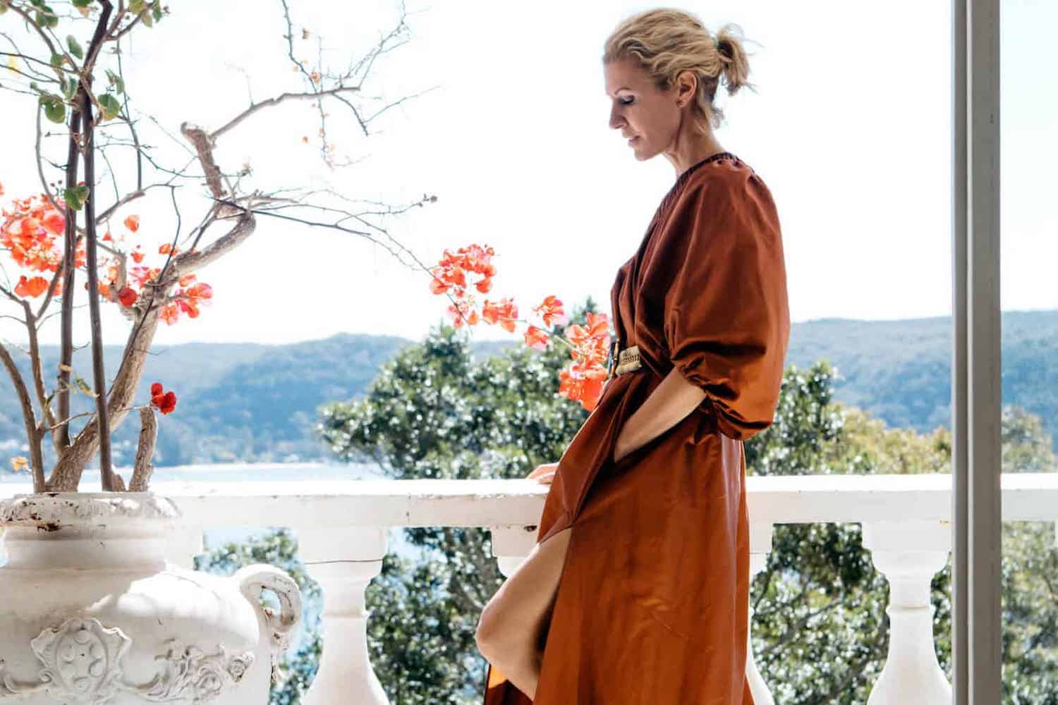 Designer Heidi Middleton in her Palm Beach villa, wearing a striped shirt and vintage Hermès skirt, standing by natural light from large windows