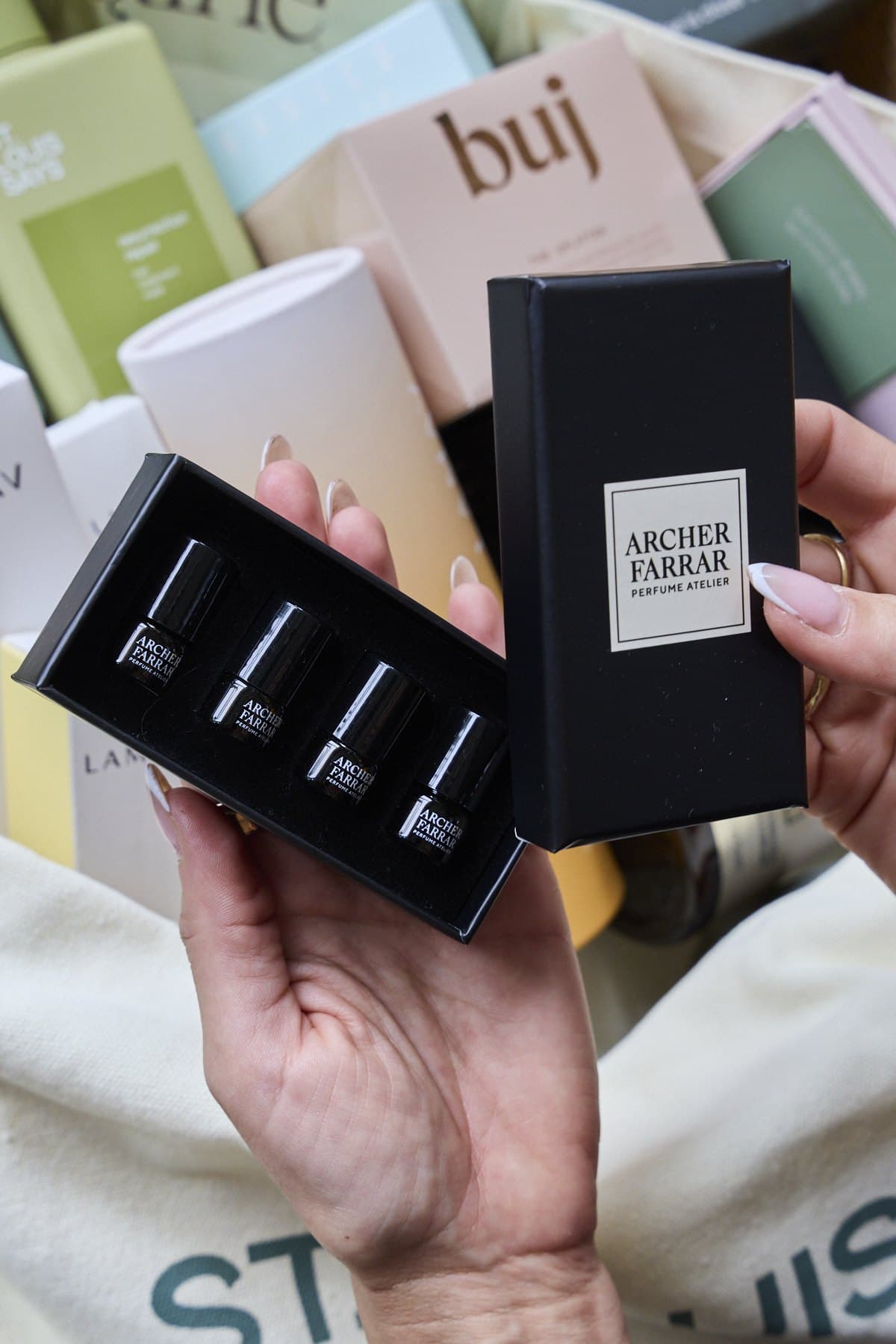 A hand holding an Archer Farrar fragrance box and buj packaging over a St. Louis Says tote