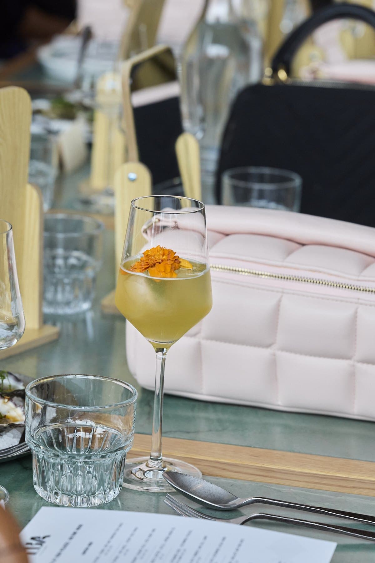 A cocktail garnished with an orange flower beside a pink quilted bag and a Lua menu