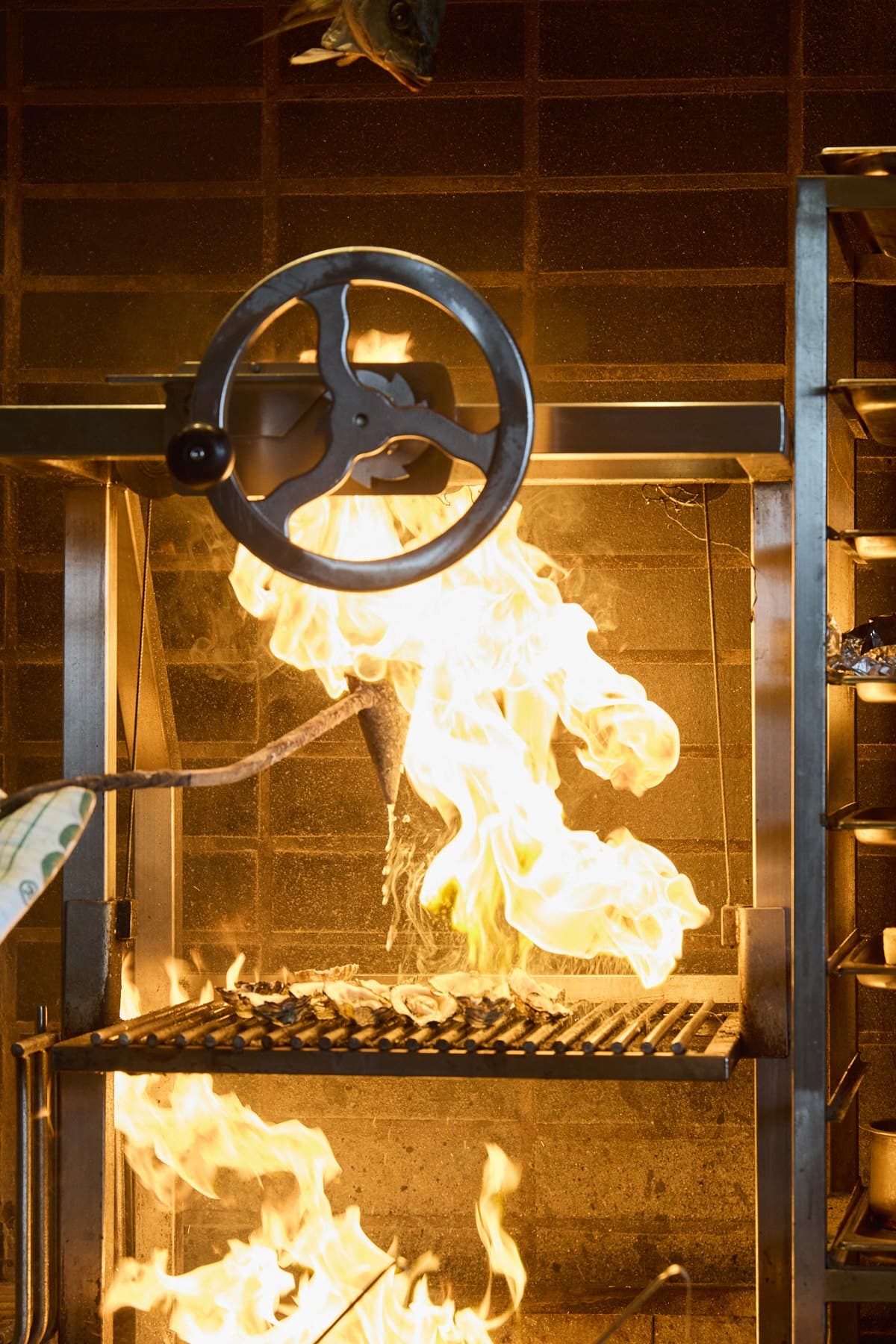 Tall flames rising at Lua's charcoal grill, with the grill wheel above