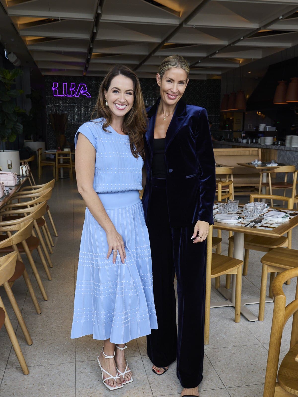 Sigourney Cantelo in a blue knit dress with a guest at Lua, Sydney Fish Market, under the neon Lua sign