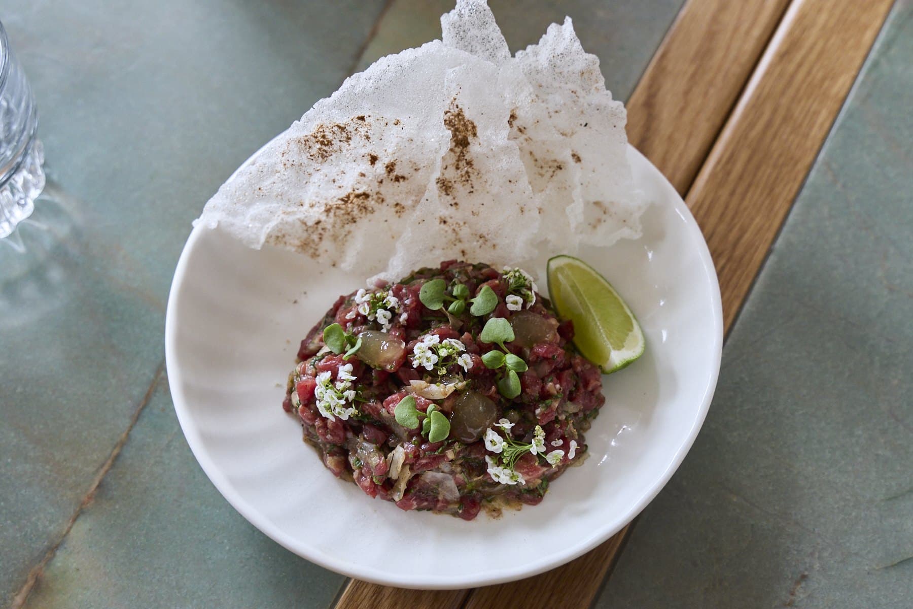 Wagyu pho tartare in a white bowl with a rice paper crisp and a wedge of lime