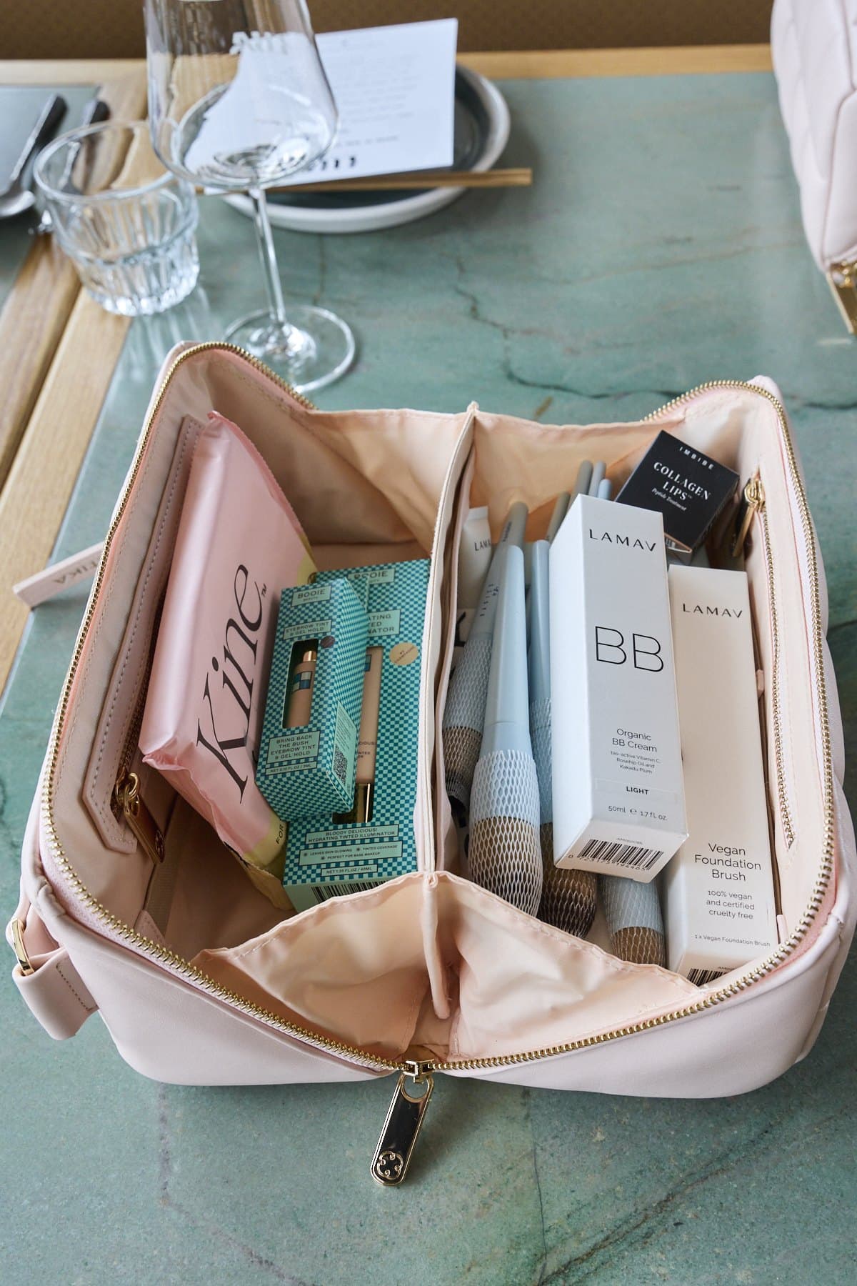 An open pink Estetika makeup bag on the table, filled with LAMAV, Kine and other products