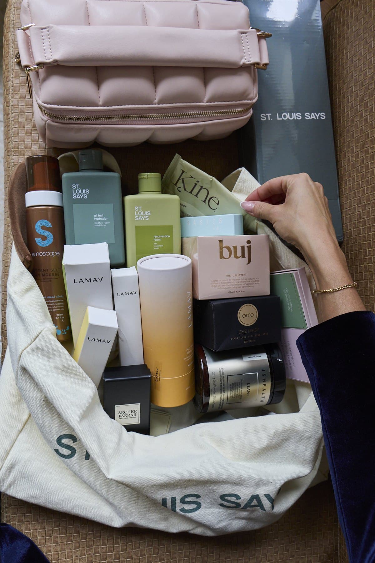 A St. Louis Says tote filled with gifts from the shop brands, beside a pink quilted bag, seen from above
