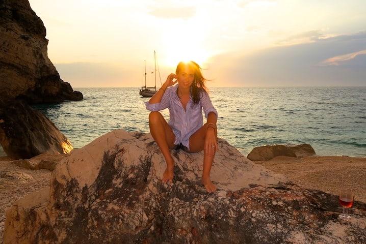 Woman on a luxury yacht in Greece with clear blue water, applying natural skincare products