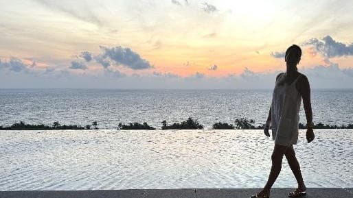 Sigourney Cantelo silhouetted against a sunset sky, walking along the edge of an infinity pool overlooking the sea at the Regent Phu Quoc in Vietnam, for Beautiful Inside by Beauticate