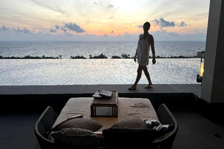 Sigourney Cantelo silhouetted against a sunset sky, walking along the edge of an infinity pool overlooking the sea at the Regent Phu Quoc in Vietnam, for Beautiful Inside by Beauticate