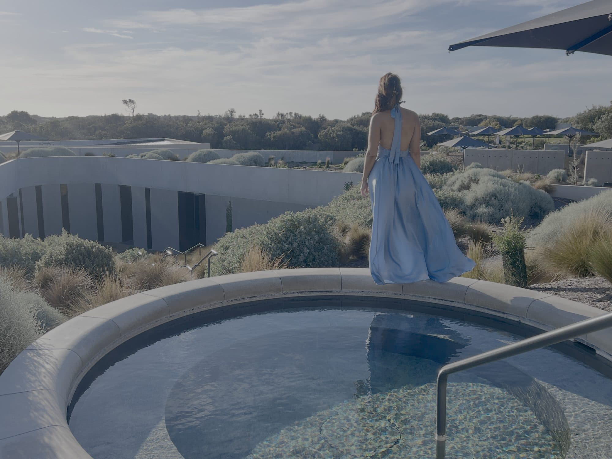 Sigourney Cantelo in a blue dress beside the rooftop thermal pool at Alba, for Beautiful Inside by Beauticate
