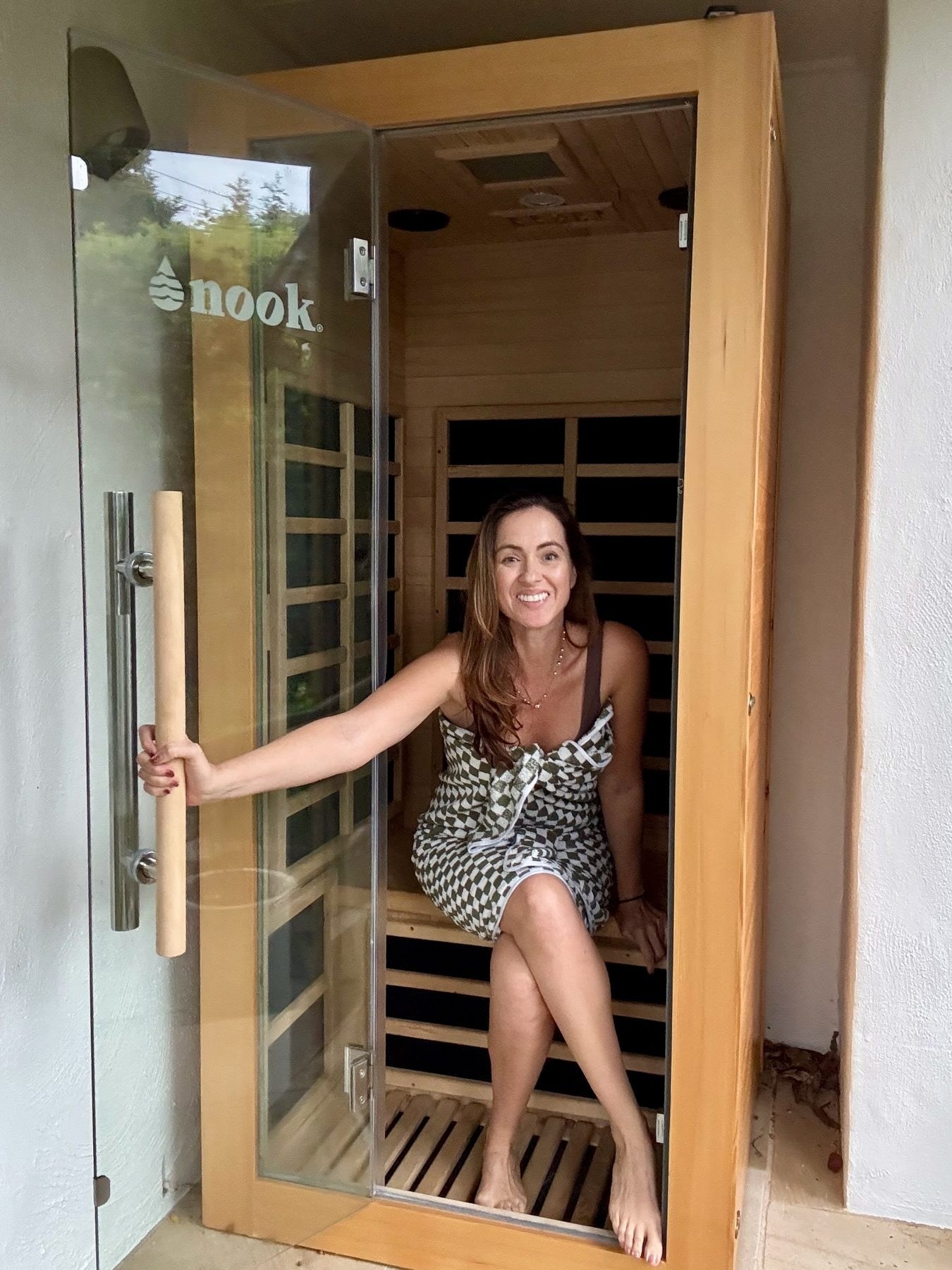 Sigourney Cantelo smiling in the open doorway of her Nook Elite infrared sauna, holding the door handle