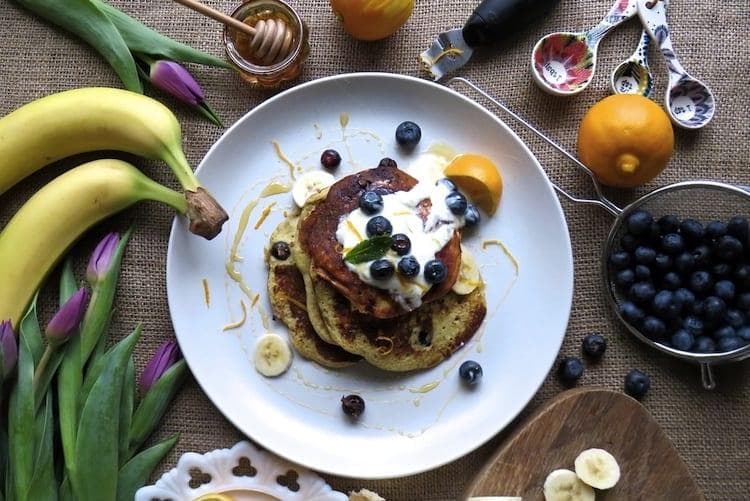 Stack of golden gluten-free banana blueberry pancakes topped with fresh blueberries, yoghurt and lemon zest