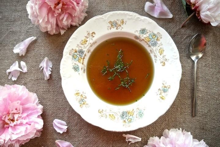 Steaming bowl of golden bone broth with fresh herbs and beetroot noodles