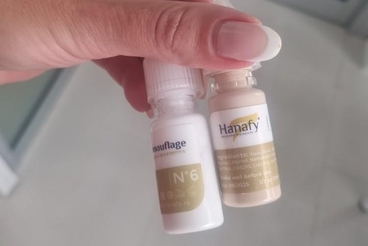 Hand holding two small vials of Hanafy camouflage pigment used for under-eye concealer tattooing