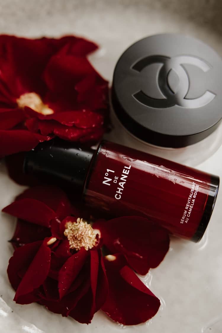 No 1 de Chanel Revitalising Serum bottle surrounded by red camellia petals