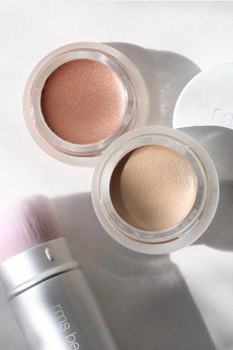 Two open RMS Beauty shimmer pots in rose-gold and champagne beside a silver kabuki brush