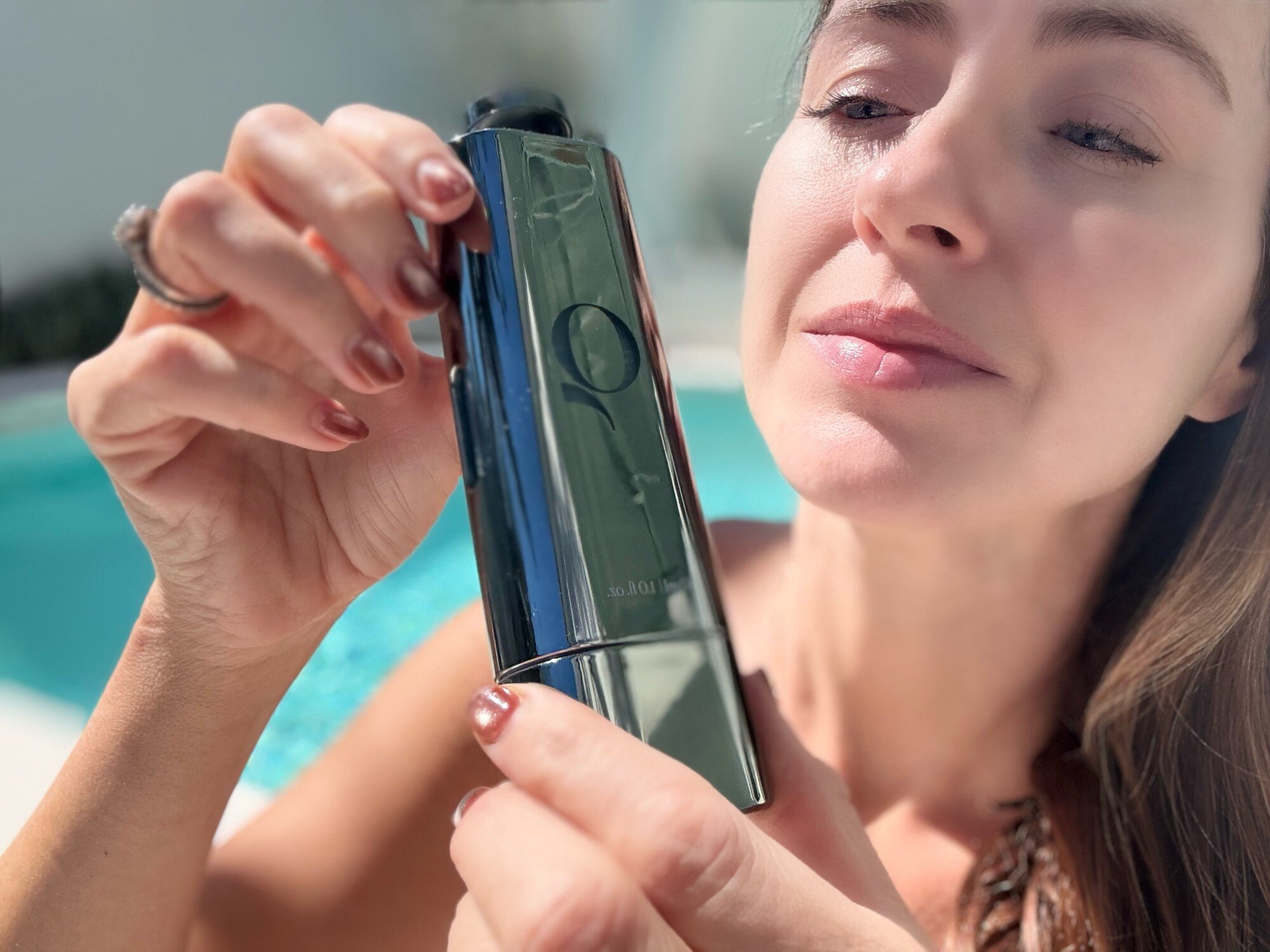 The Qure Blue+ Face Serum held up against the pool, its deep blue formula visible through the bottle