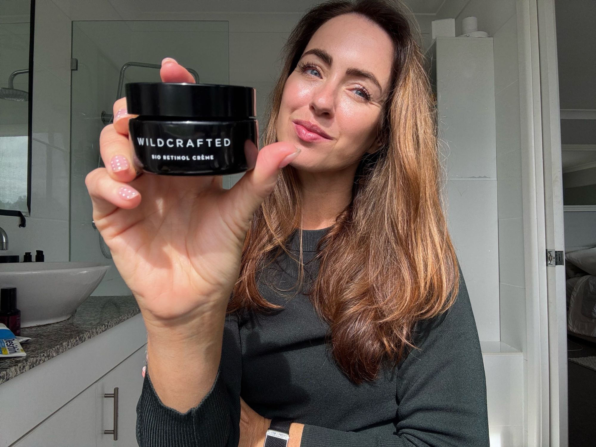 Sigourney in her bathroom holding up the Wildcrafted Organics Bio Retinol Crème jar
