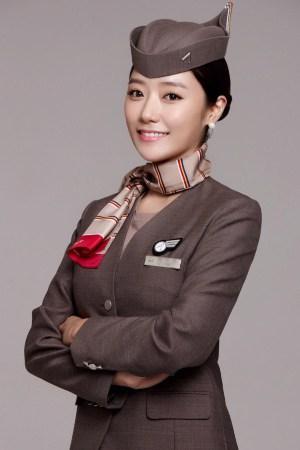 Korean Air flight attendant in a taupe uniform and pillbox hat posing with arms crossed