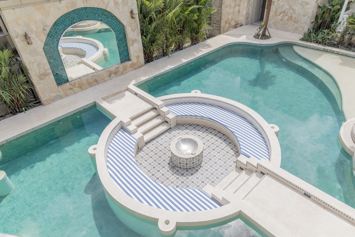 The sunken fire pit at Escape Haven seen from above, blue striped banquettes ringing a tiled circle set into the pool