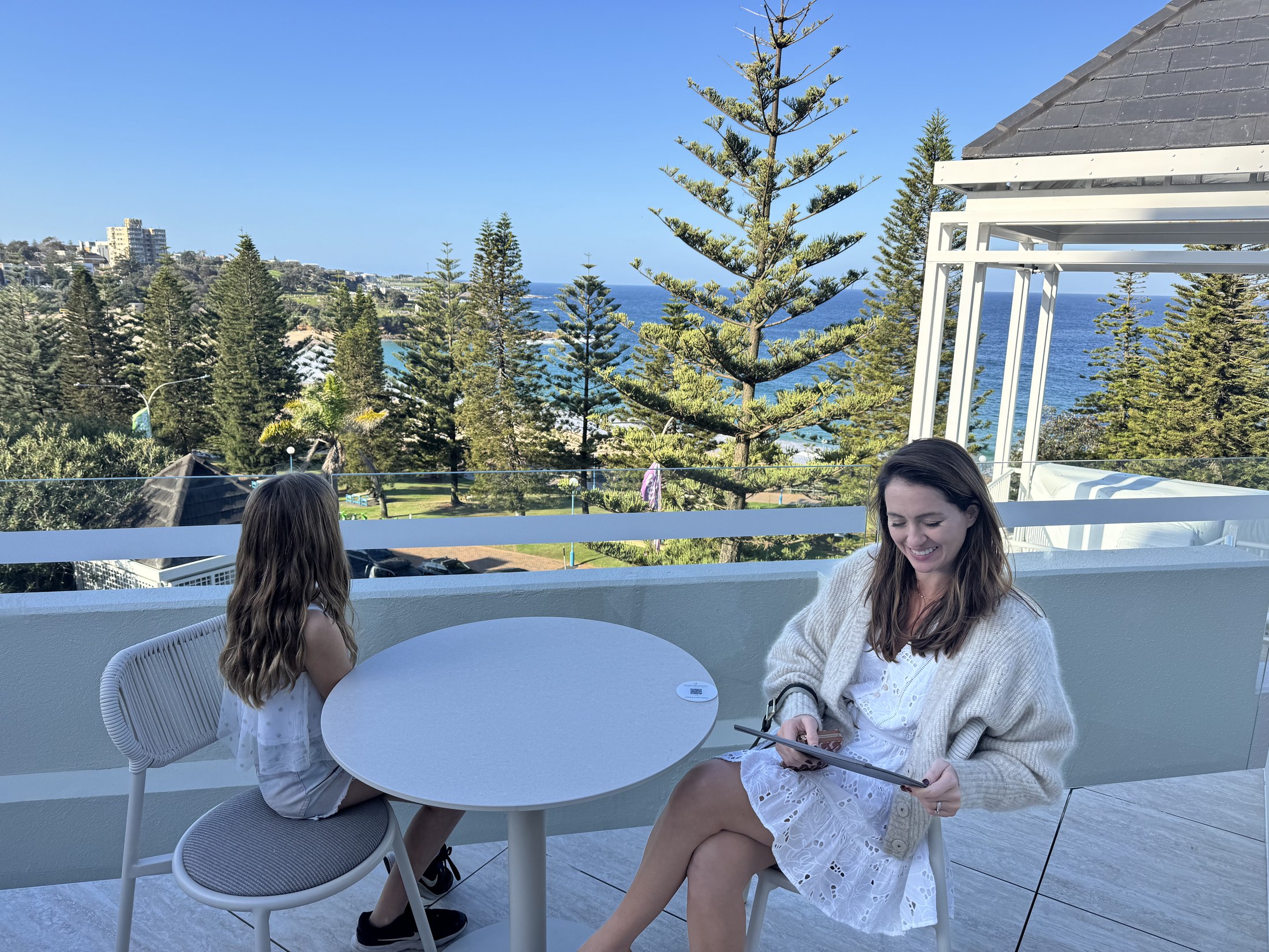 Sigourney and Lulu on the Club lounge terrace, Coogee Beach and the Norfolk pines behind them