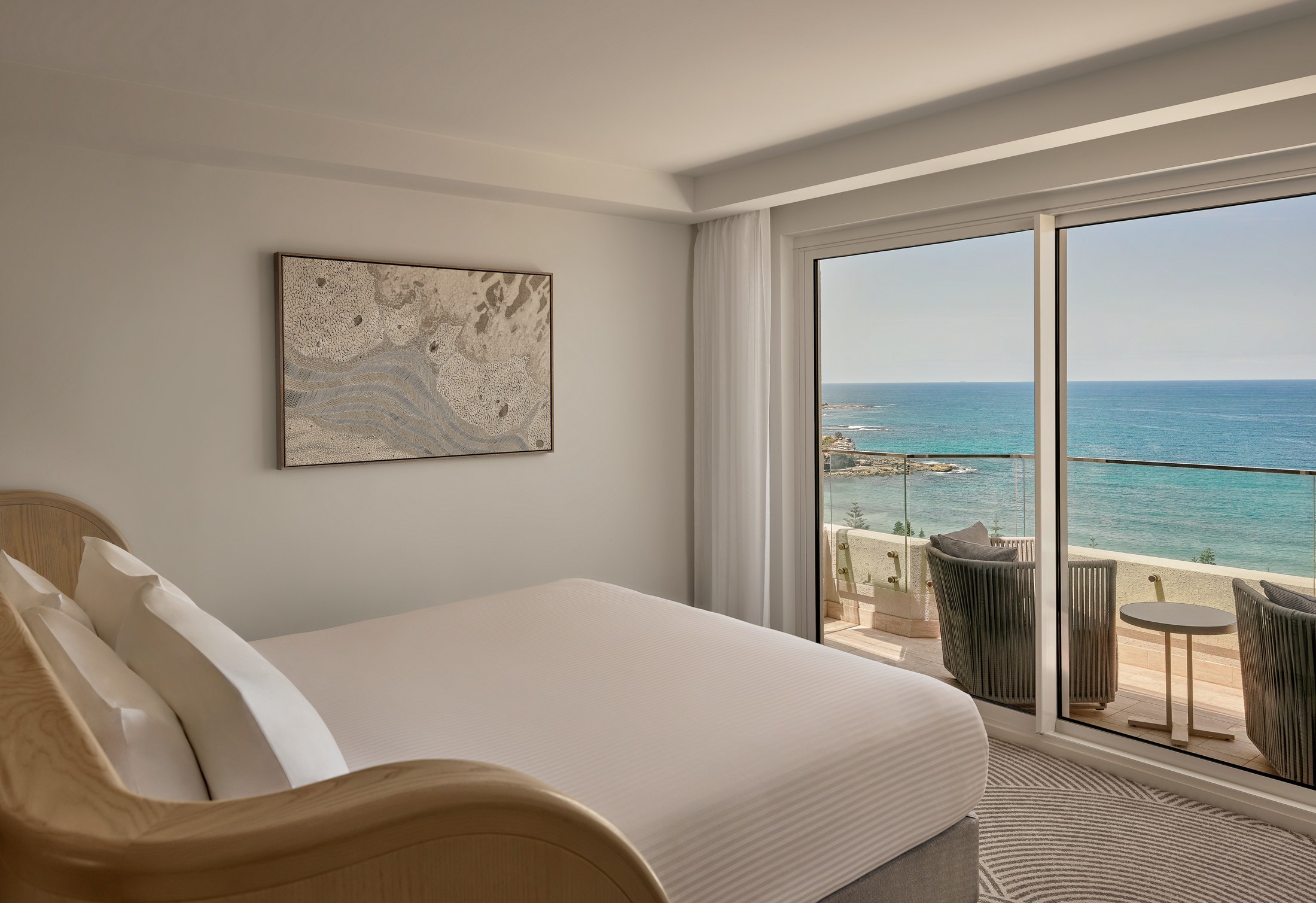 An ocean front room at InterContinental Sydney Coogee Beach, white and cream with floor to ceiling glass opening onto the beach view