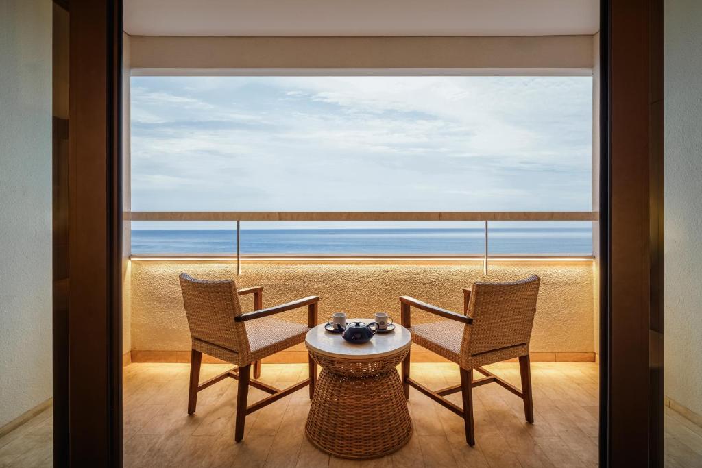 View from a hotel balcony overlooking lush tropical gardens and the Sanur coastline, with traditional Balinese architecture in the foreground