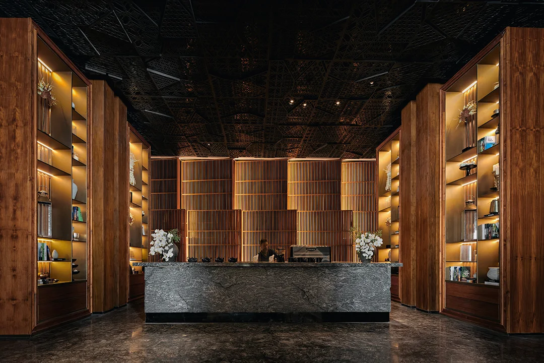 The lobby bar at The Meru Sanur with carved ceilings, dramatic lighting, bookshelves and sculptures amid lush living spaces