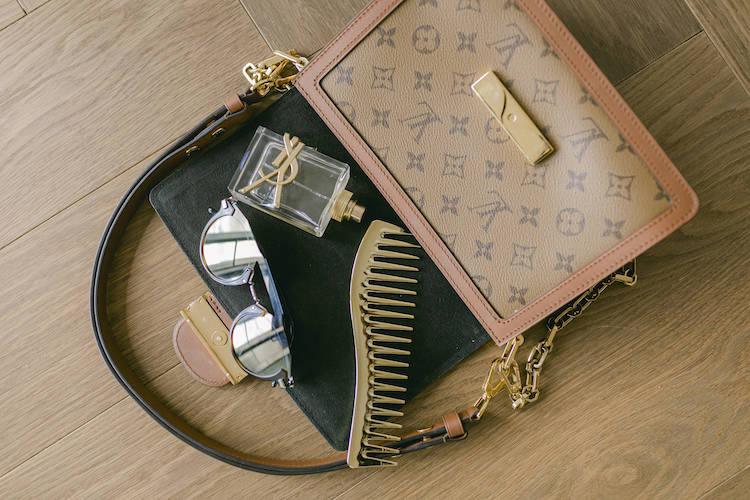 Louis Vuitton monogram handbag flat lay with perfume, sunglasses, hair claw clip and gold lighter