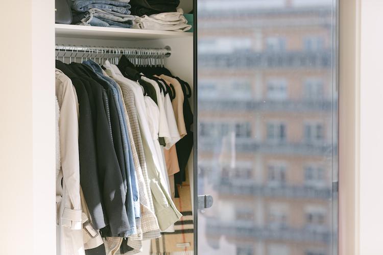 Organised wardrobe with folded denim and hanging shirts behind glass, city building reflected in door