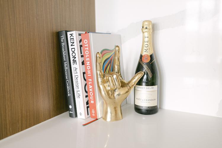 Coffee table books, a gold shaka-hand sculpture and a personalised Moet bottle on a white shelf