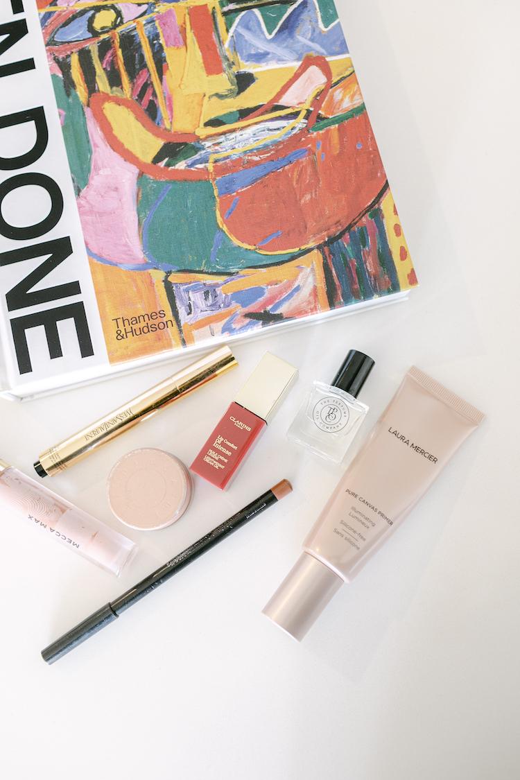 Flat lay on a Ken Done art book: Clarins lip oil, Laura Mercier primer, perfume, liner and mascara