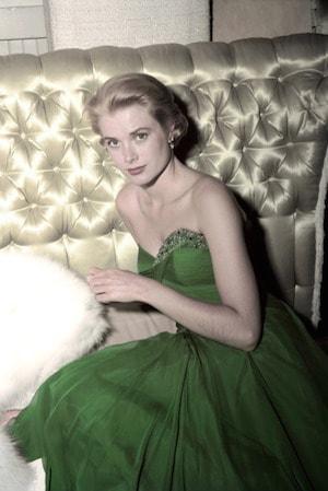 Grace Kelly seated against tufted satin, wearing an emerald-green strapless gown with a white fur wrap